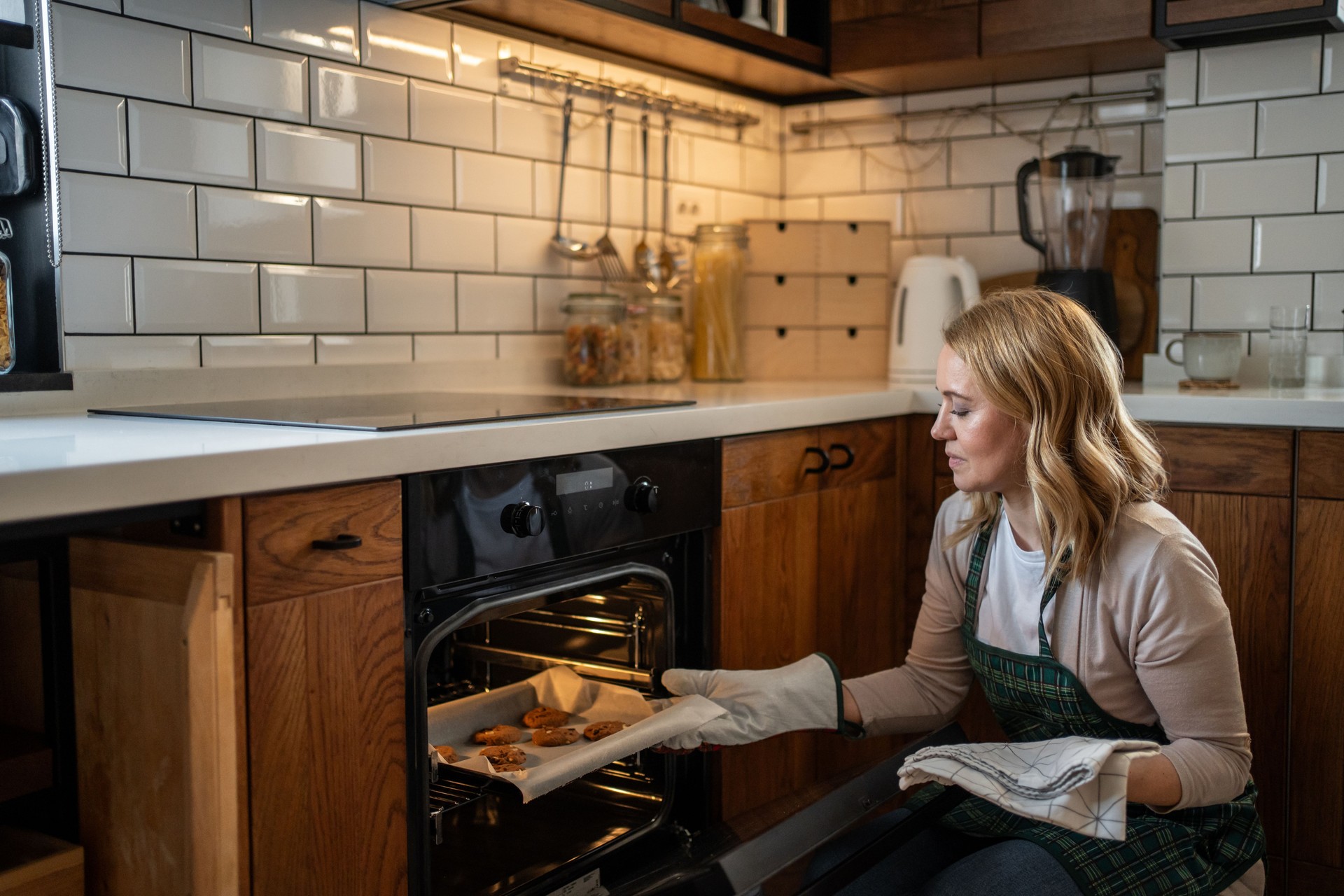 Woman baking cookies in modern kitchen: taking tray out of oven